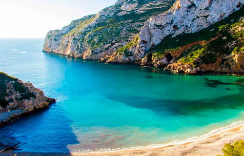 A breathtaking view of Javea's natural beauty, with crystal clear blue and green water and lush greenery in the background.